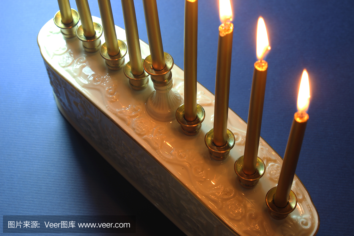 白色陶瓷烛台的局部视图与金色蜡烛在蓝色背景下,背光