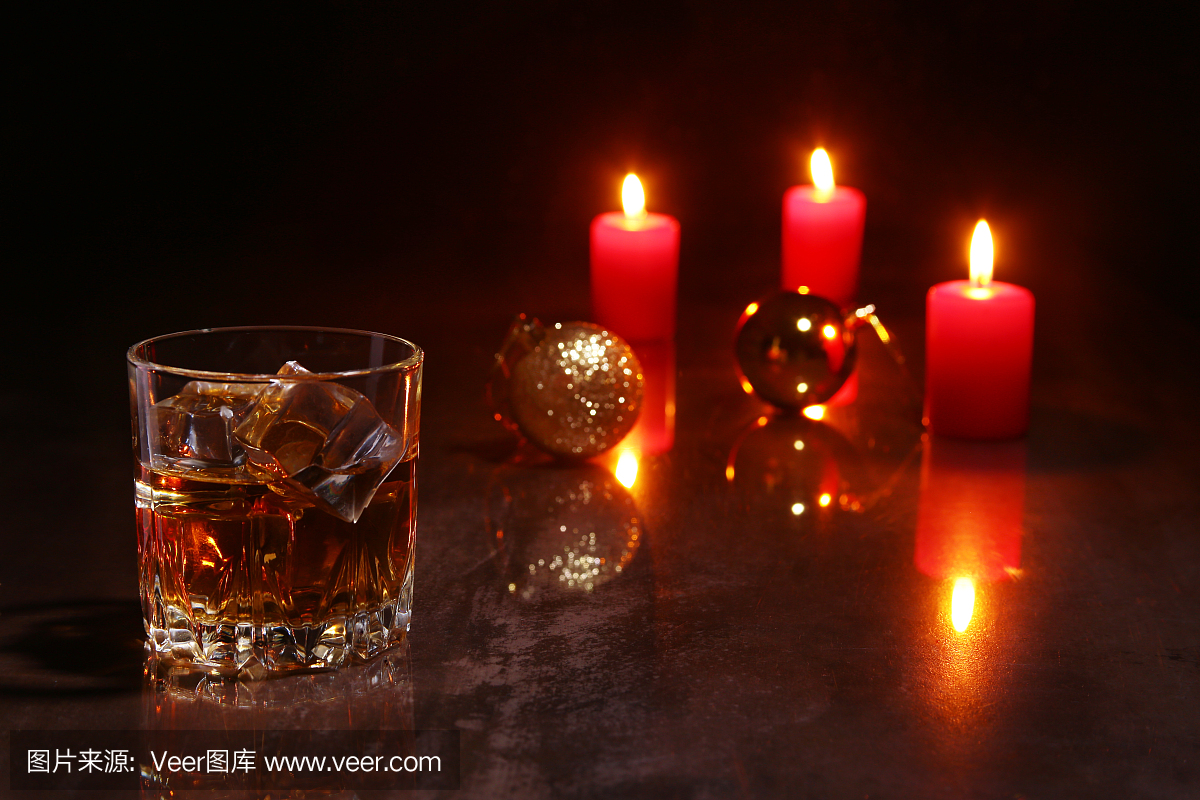圣诞装饰。一杯白兰地或威士忌,红色的蜡烛和彩色的球在木制的背景。